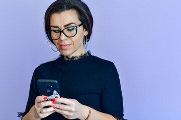 Cheerful Smiling Woman in Eyeglasses looking at the phone  reading a Message ,checking social media, shopping online,  ordering delivery  against pink wall, connected to high speed internet