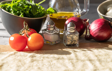 Topping ingredients for a tarte flambe of appetizing arugula, tomatoes, onions, mushrooms, peppers, mozzarella and spice jars on a gray background.