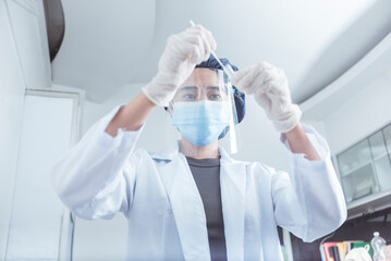 A laboratory technician inserts a covid nose swab into a tube for testing. RT-PCR test procedure. Wearing face shield for extra precaution.