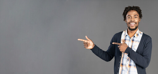 Pointing or directing young african american man in dark navy jumper with both hands turn sideways looking at camera and smile, isolated on grey background. Elegant male model in studio. copy space. 