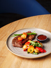 Grilled steak with vegetables and sauce. Juicy steak with tomatoes, potatoes, peppers and green beans in a plate on a wooden background. Delicious hearty lunch. Meat with baked vegetables. Close up.