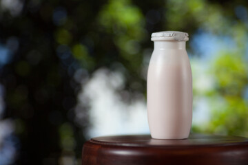 Natural liquid yogurt with probiotics in small plastic bottles on wooden table on background of green trees on a sunny day. Healthy, balanced diet food, healthy breakfast, dairy products.