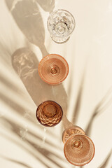 Set colored glasses from transparent and beige glass with beautiful shadows from palm leaf at...