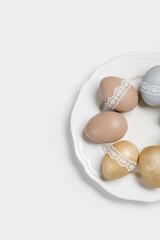 Dyed Easter eggs pastel colors golden, gray, beige on white plate. Happy Easter holiday, celebration food concept, chicken egg neutral trendy color and decorated lace tape. Top view table
