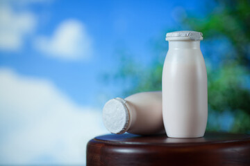 Natural liquid yogurt with probiotics in small plastic bottles on wooden table on background of blue sky with clouds. Healthy, balanced diet food, healthy breakfast, dairy products.