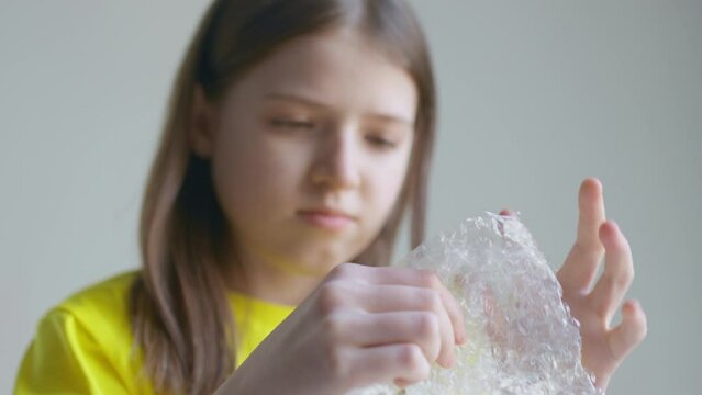A blonde teenager girl in a yellow T-shirt bursts bubble wrap and is bored