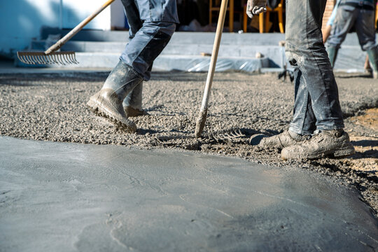 Workers walking on top of the concrete, spreading it with manual shovels, while the concrete stays fresh