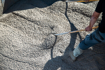 .Workers in the sun spreading the concrete with rakes inside the pool, repairing it for the summer