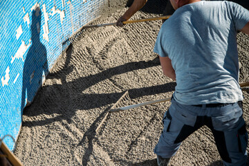 Workers in the sun spreading the concrete with rakes inside the pool, preparing the garden part - obrazy, fototapety, plakaty