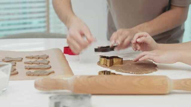Close-up Of Mother And Her Daughter Making Homemade Gingerbread Cookies In Kitchen. Daughter Helps Her Mother Сarving Cookie Out Of Dough