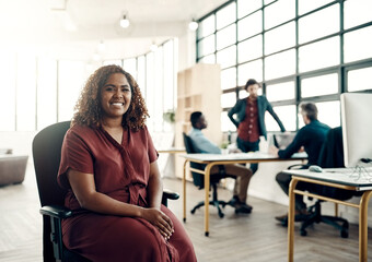 Positivity is the key to success. Portrait of a young businesswoman sitting in a modern office with her colleagues working in the background.