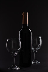 Dark wine bottle with two empty glasses on a black background, perfect for wineries and beverage promotions.