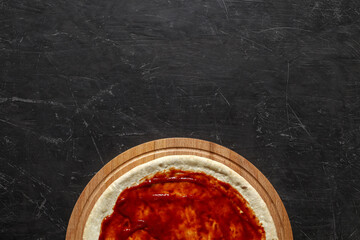 Tomato sauce is spread on round pizza dough, op view dark background, with space to copy text.