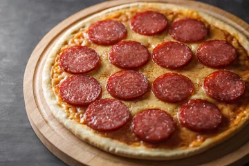 Foto op Plexiglas Pepperoni pizza uncut on wooden stand on dark background, selective focus. © elenvd