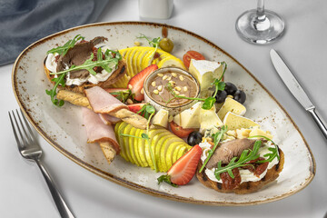 banquet dish with sliced pears, cheeses and tomatoes, with bruschettas with roast beef, cream sauce, sun-dried tomatoes and arugula, with bread sticks in ham. 