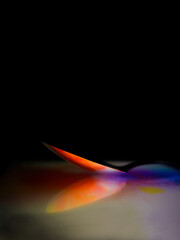 Metal spoon on the reflecting surface in the black background. Play of colors in orange and violet