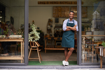 Proud of my shop. A handsome young man standing in the entrance to his store.