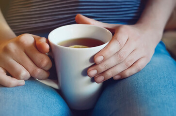 White glass of tea with lemon in the hands of a girl close-up. The concept of warmth, comfort and coziness. Blurred photo, soft focus.