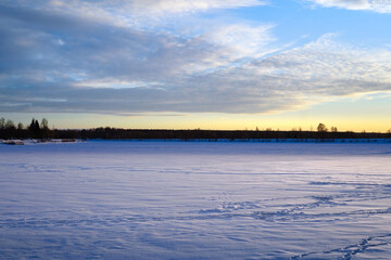 View of the part of the Volga River frozen and covered with a thick layer of snow during the January sunset. Fishermen's footprints are visible in the snow.