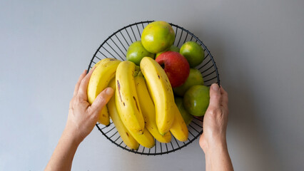 hands holding fruit basket. Orange, apple, banana, mango, lemon.