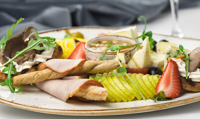banquet dish with sliced pears, cheeses and tomatoes, with bruschettas with roast beef, cream cheese, sun-dried tomatoes and arugula, with bread sticks in ham. 