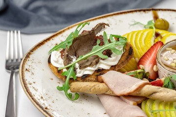 bruschetta with roast beef, butter cream and arugula lies on a banquet dish, next to it are sliced lemon, pear and strawberry, breadsticks in ham, close-up