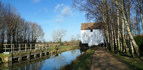 Fototapeta na wymiar Watermill and Mill stream at Lode in Cambridgeshire with trees and blue sky.