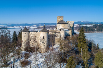 Naklejka premium Poland. Medieval castle in Niedzica, dating back to 14th century (upper castle) in winter. Frozen artificial Czorsztyn lake on Dunajec river.