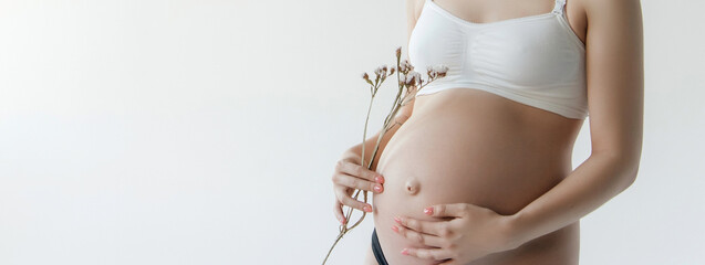 Woman standing and touching with hands her naked big belly. Isolated on gray background. Emotional loving pregnancy time - 37 weeks. Baby expectation. Love, happiness and safety concept. Closeup