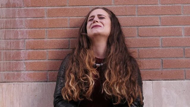 Girl cries leaning against the wall