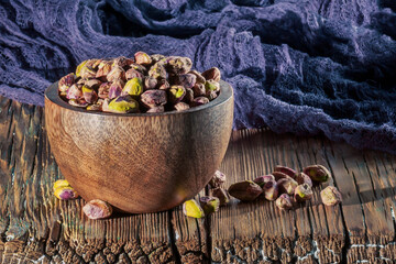 Peeled pistachios in a bowl on a wooden background.