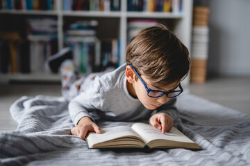 One caucasian boy lying on the floor at home in day reading a book front view copy space real...