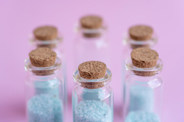 6 botellitas de cristal con tapa de corcho con relleno de piedritas color turquesa y fondo liso de color rosado  y desenfoque del fondo