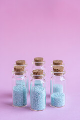 6 botellitas de cristal con tapa de corcho con relleno de piedritas color turquesa y fondo liso de color rosado  y desenfoque del fondo