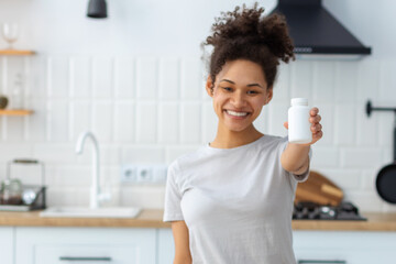Happy young African American woman holding bottle of dietary supplements or vitamins in her hands....
