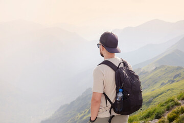 A bearded traveler with a backpack on the top of a mountain. A tourist with a backpack stands the background of a mountain. 