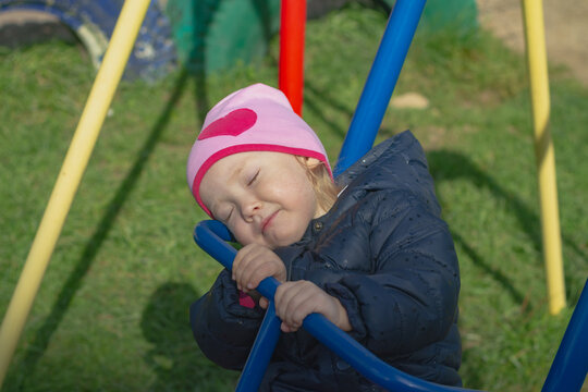 The Caucasian Baby Girl Sleeps And Swings On A Swing In Spring Or Autumn In The Rays Of The Warm Sun