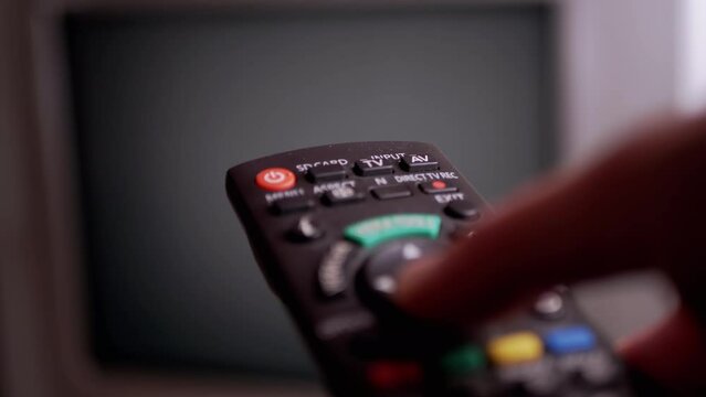 A Male Hand Holds a Remote Controller and Switches Flickering Channels on Screen. Interference. Pressing buttons, bad signal transmission, watching old TV. Black and white noise. Blurred background.