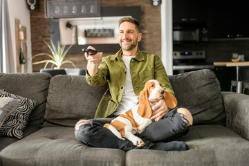 Man Playing With basset Pet Dog At Home sofa listening TV