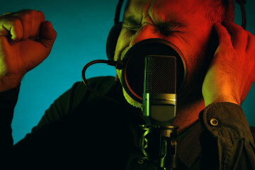 Portrait of a middle aged man wearing headphones and singing into a microphone, isolated on green...