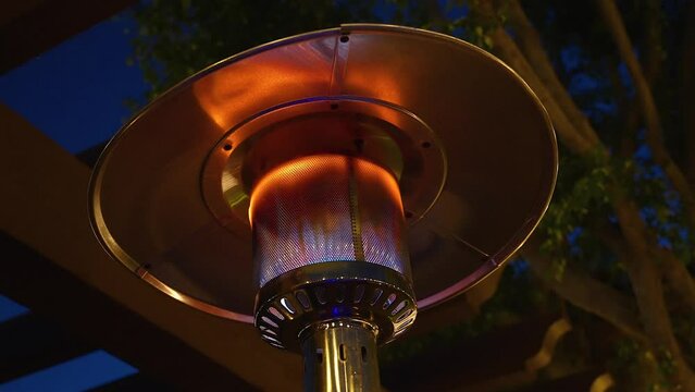 Outdoor propane heater glowing under a tree late evening