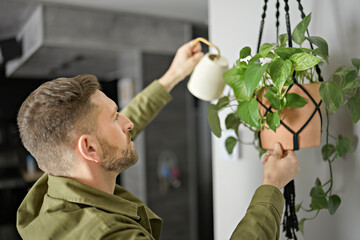 A nice Man spraying water on a house plant and flower with a spray bottle at home