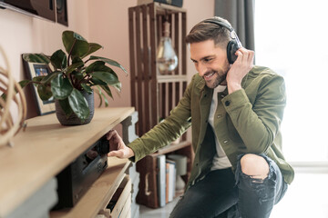 Handsome guy wearing headphones enjoys music in front of his stereo system - obrazy, fototapety, plakaty