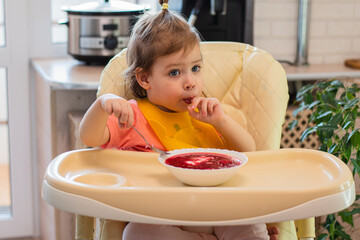 A small child eats vegetable soup with a spoon while sitting on a high chair