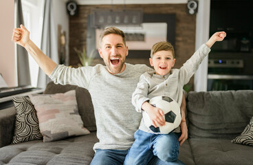 Soccer fans Emotional dad and son cheering with football ball, watching sport on tv at home