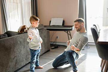 Happy father and little son having fun together in living room play air guitar