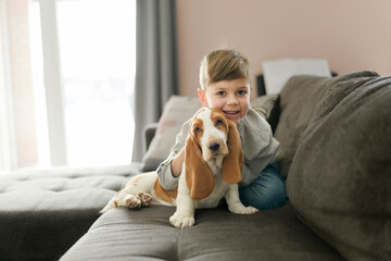 Happy kid in living room at home with Basset dog