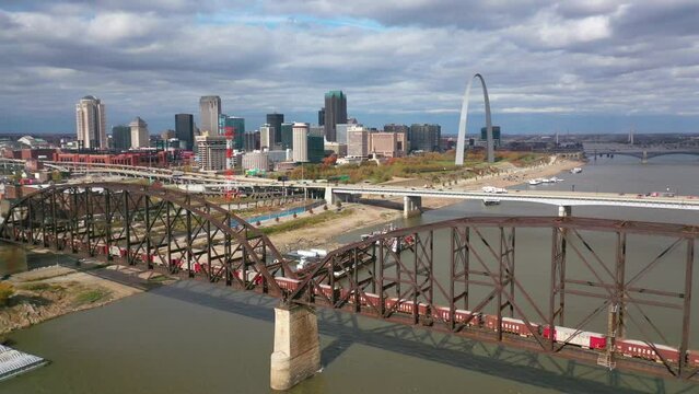Aerial of a freight train crossing the Mississippi River with the St. Louis Gateway Arch and city skyline background.