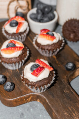 Chocolate muffin cupcakes. Cream cheese, a blueberry and sliced strawberry. Selective focus shot.