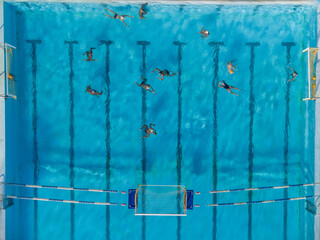 Aerial drone top view shot of people competing in water polo in turquoise water pool